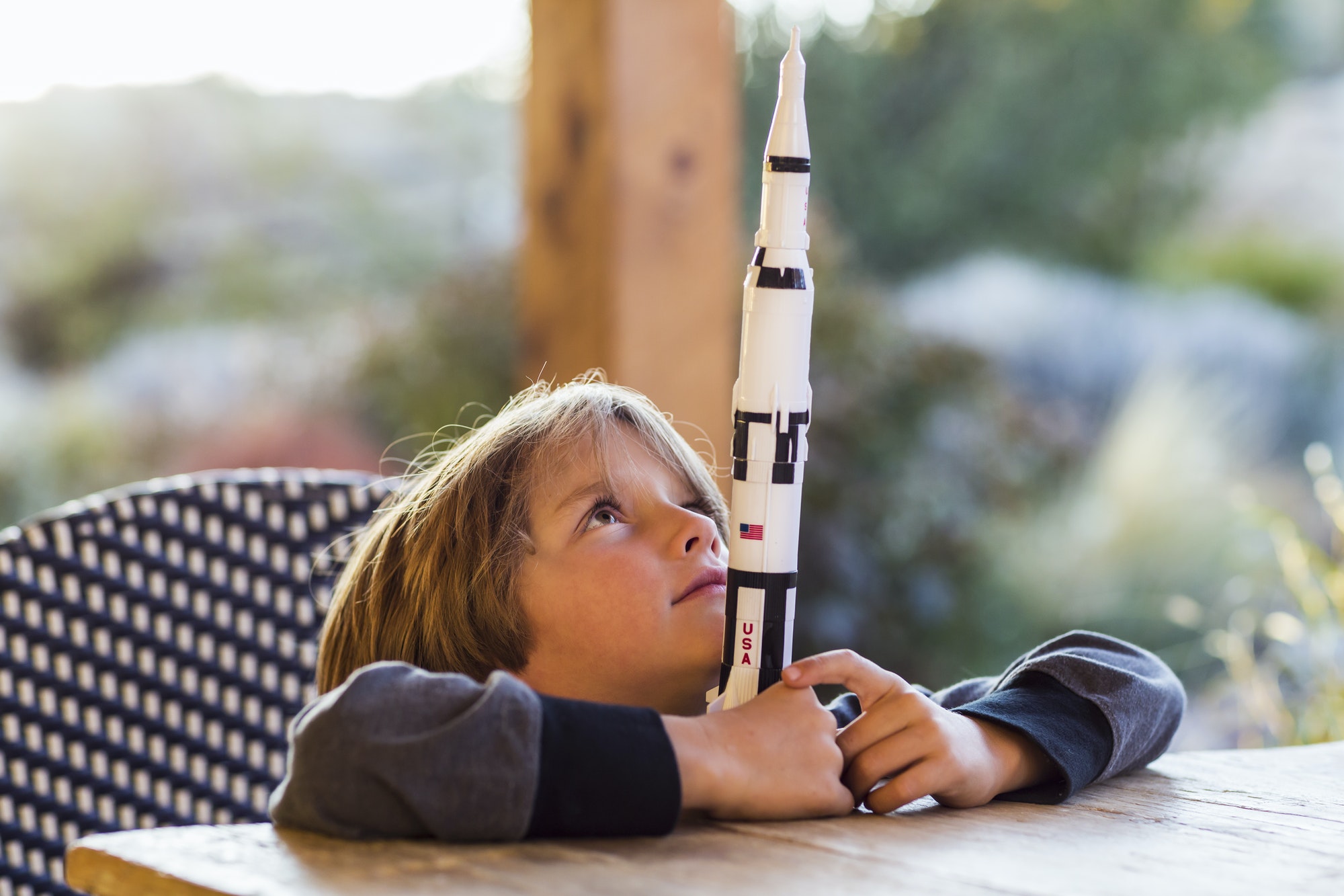 A boy playing with a toy Nasa Saturn 5 rocket, day dreaming about space flight.