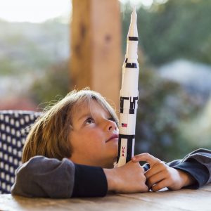 A boy playing with a toy Nasa Saturn 5 rocket, day dreaming about space flight.